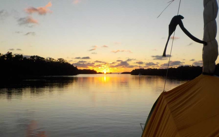 the sun rises or sets behind a body of calm water